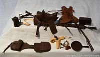 Photo showing assortment of toy cowboy accessories including saddle, rifle, chaps, pistol, skillet, and handcuffs spread out on white surface.