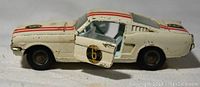 Side view of white diecast Ford Mustang 2+2 model car with red stripes and open driver's door showing number 6 decals on door and side, worn paint visible