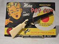 Front view of miniature pop gun and original card with coloring and branding visible