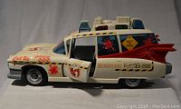Side view of the Ghostbusters Cadillac ambulance toy showing open front door, rear side window, decals with warnings and logo, and red tail fins