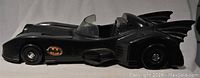 Side view of the black plastic Batmobile toy car with visible Batman logo and bat wing details.