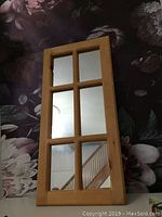 Front view of the wooden framed mirror showing the divided glass panels with a floral backdrop.