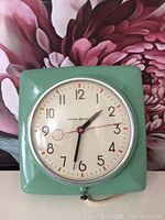 Front view of vintage green General Electric wall clock showing clock face, hands, and green square plastic case.