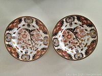 Pair of Royal Crown Derby plates with intricate floral and ornamental border patterns, showing top view of both plates side by side.