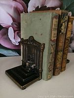Metal bookend holding vintage books, showing overall design and size relative to books