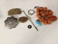 Full view of all items in the lot including belt buckles, compact, watch, necklace and coin/token.