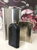 Lot of three flasks including a large stainless steel flask, a hammered metal flask, and a smaller vintage leather covered flask