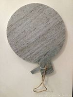 Top view of the round marble cutting board showing gray marble surface with delicate veining, round shape with an attached handle at bottom.