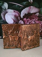Pair of vintage copper bookends shown side by side, showing embossed stags and forest background