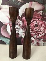 Front view of two tall dark wood mid century modern candle holders placed side by side.
