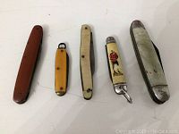 Five vintage small pocket knives laid side by side showing handles.