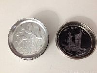 Photo showing one duck motif metal coaster (silver-tone) and one Toronto New City Hall coaster with black background and white drawing.