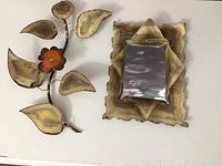 Full view of two metal decor items: floral piece on left, mirror on right on white surface.