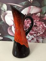 Front and side views of a vintage mid century modern pottery vase with orange, brown, and black glaze, curved handle and angular spout