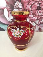 Vintage ruby glass vase with handpainted floral design and gold accents, front angle showing some wear on gold rim