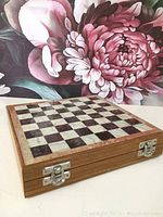 Closed view of the wooden folding chess board with metal clasps, showing the stone inlay light and dark squares on top, size about 8 inches square.
