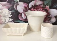 Three vintage white pottery pieces on floral background: rectangular dish, tall planter, and small embossed pot.