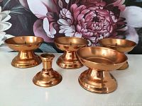 Five vintage copper candle holders arranged on a floral background, showing their range of sizes and designs.
