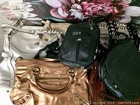 Image showing a collection of eight purses in various colors and styles including white, black, bronze, and dark green.