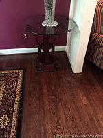 Full view of round glass table with dark wood base against a purple wall and hardwood floor, showing table setup and surroundings.