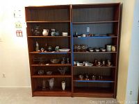 Front view of two wooden bookcases side by side with items on shelves for scale but contents not included