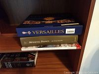 Close-up on three book titles: 'Versailles', 'Medieval France: An Encyclopedia', and another unidentified book, showing some of the hardback book subjects included.