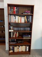 Front view of the taller bookcase filled with books and CDs to show shelf layout and condition