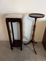 Side view of marble top square wooden side table next to round wooden plant stand showing height and design details.