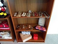 Full view of wooden shelving displaying necklaces on top shelf, earrings, bracelets, cufflinks, cosmetic bags, and decorative boxes on shelves below.