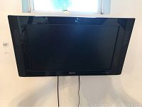 Front view of Phillips 32 inch flat screen TV mounted on wall with cables hanging down.