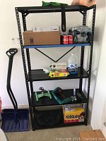 Full view of the metal shelving unit loaded with various items such as boxes, a water jug, soda cans, tools, and snow shovel leaning against side.