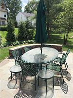 Full patio set displaying oval table, six chairs, green umbrella and two small tables outdoors on stone patio.