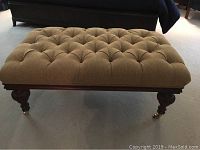 Full view of rectangular cushioned bedroom bench in brown tufted fabric on four dark wood turned legs with brass casters.