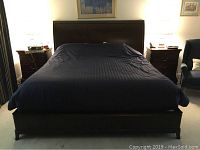 Front view of the king size wooden bed frame with headboard covered with a dark bed cover. Wooden frame is visible at the base and headboard.