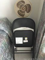 Black padded metal folding chair showing back and seat with label