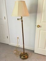 Full view of the floor lamp, showing entire lamp height with brass base and beige shade.