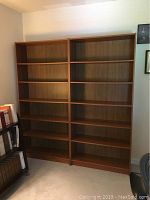 Two matching tall wooden bookshelves side by side in a room, each with six shelves and a warm brown finish.