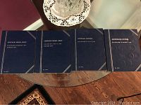 Four blue coin collection binders on glass table including two Lincoln Head Cent albums, one Buffalo Nickel album, and one Jefferson Nickel album.