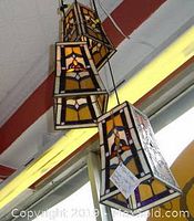 Photo of three stained glass rectangular hanging lamps with geometric design, suspended from ceiling.
