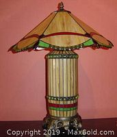 Table lamp showing stained glass shade and decorative metal base against an orange background.