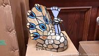 Photo of single loose peacock stained glass night light lamp showing front and detail of stained glass design.