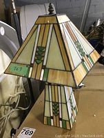 Single stained glass style table lamp showing the geometric cream, green, and amber panels on the shade and base with dark metal trim.