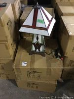 Photo of one of three Tiffany style stained glass table lamps sitting on cardboard boxes with visible power cord.