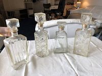 Four glass liquor decanters with stoppers on white cloth in living room setting
