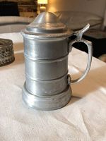 Photo of a pewter beer stein with hinged lid and handle, showing cylindrical body with bands.