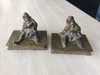 Pair of brass bookends showing a man with sleeping gown and night cap seated holding a book, each on a rectangular base.