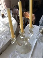 Clear glass candelabra holding three beige candles on a table.