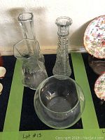 Four assorted clear glass vases against a wall, showing different shapes including hexagonal, fluted tall, round globe, and tapered cylindrical.