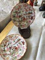 Photo showing two hand painted Asian china plates placed on wooden holders, capturing the intricate details and colors of the plates and the holders.