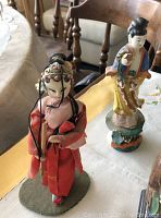 Two porcelain Geisha figurines placed on a table, showing detailed attire and facial features.